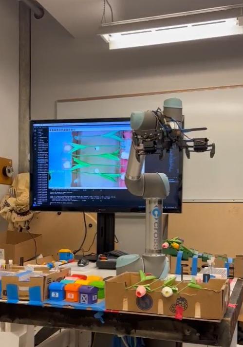 UR5 arm reaching over the tulip kitting station, with the live YOLO detection overlay visible on the monitor behind it
